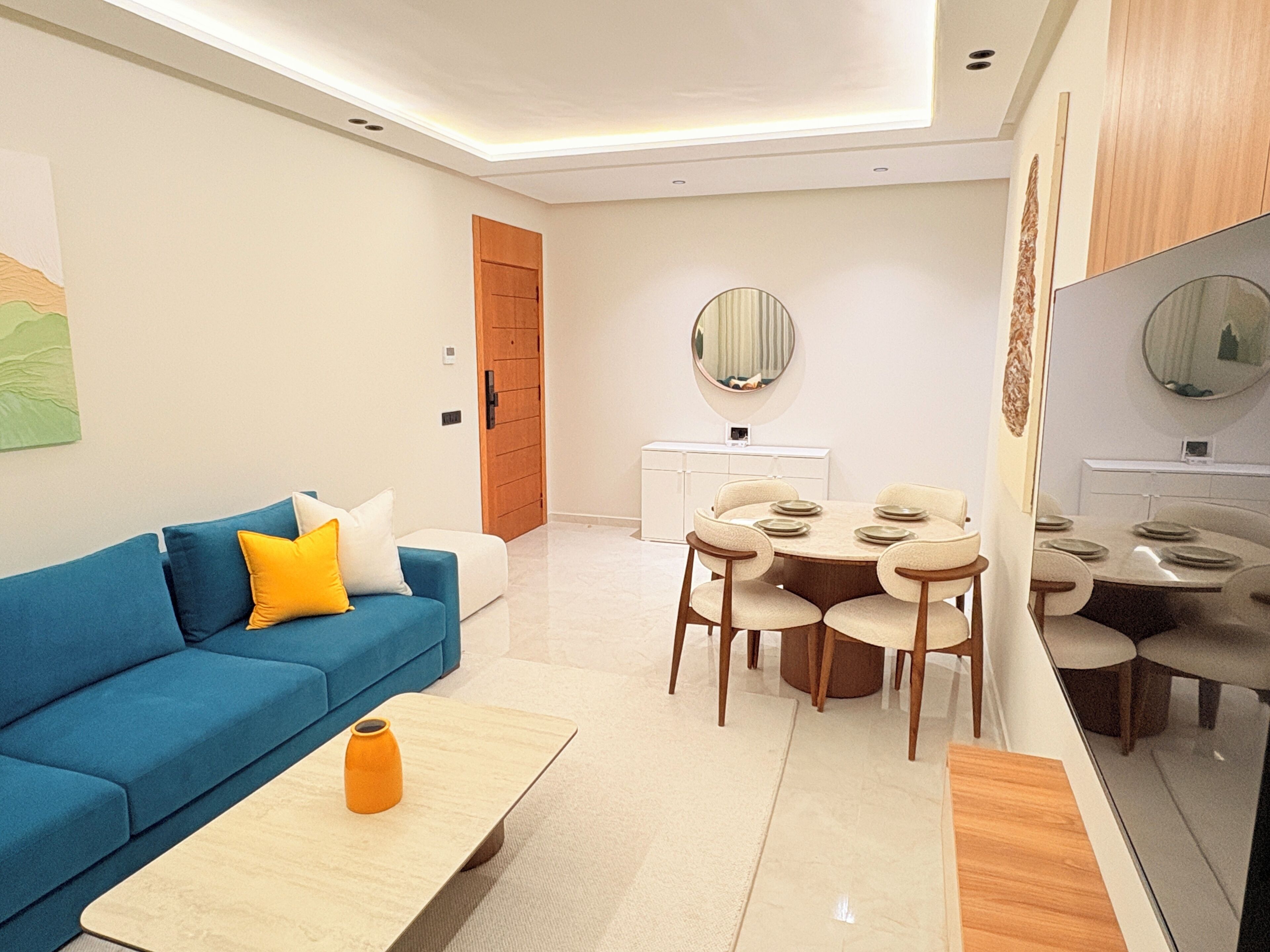 Un salón moderno con un sofá azul, una mesa de centro y un comedor con una mesa redonda y sillas.