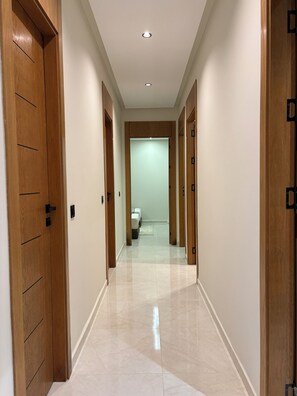 Un pasillo con puertas de madera, piso de baldosas y una lámpara en el techo.
