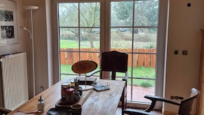 A dining area with a wooden table, chairs, a sign reading 'Jägerstube,' and a view of a garden through large windows. - Apartment 'Jagdhaus An Der Nemitzer Heide' with Wi-Fi (Prezelle)