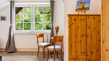 Een kamer met een raam, twee stoelen, een houten kast en een schilderij aan de muur.