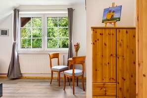 A room with a window, two chairs, a wooden cabinet, and a painting on the wall.