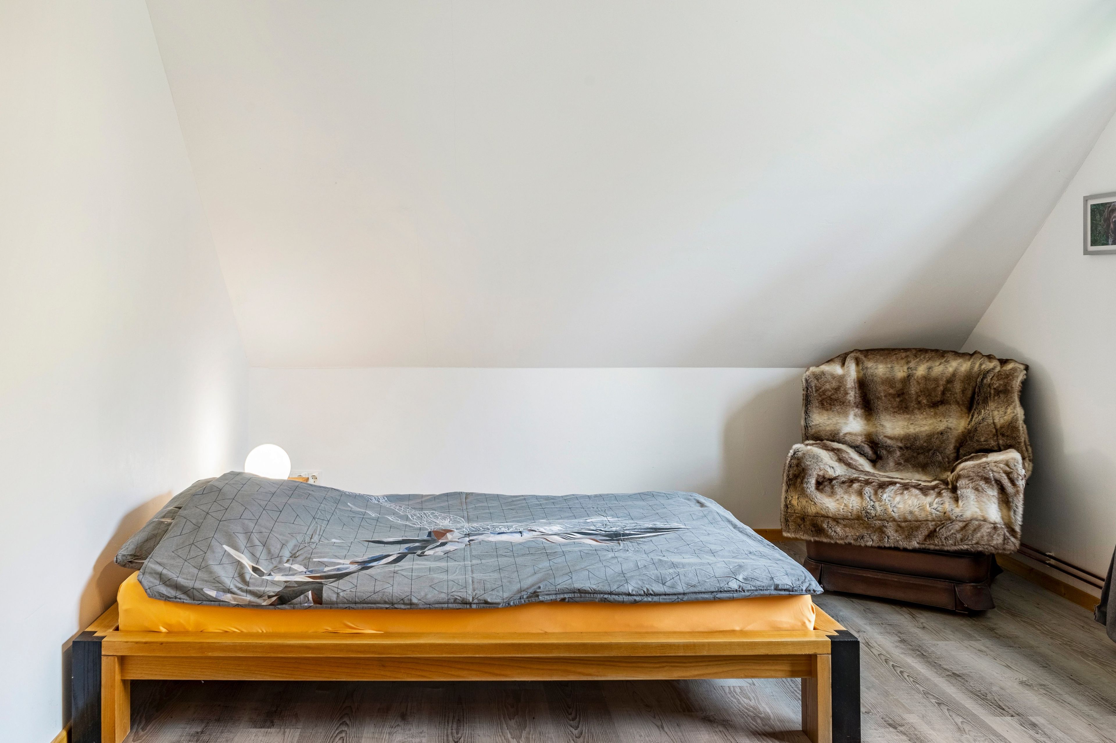 Ein Einzelbett mit einem Kissen mit geometrischem Muster und einem Holzkopfstück in einem Raum mit schrägen Wänden.