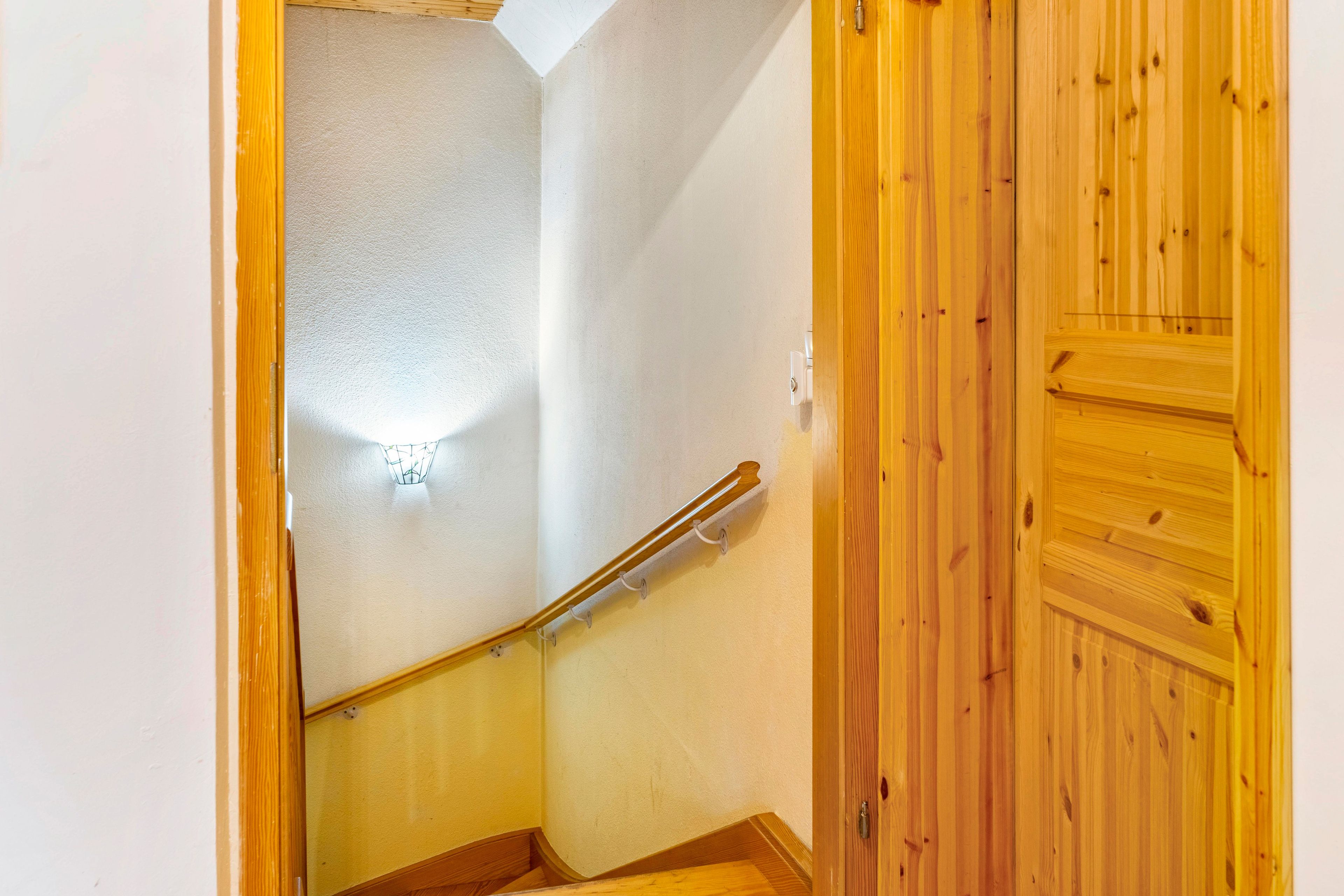 Una escalera de madera con barandilla, un aplique de pared y una puerta de madera.