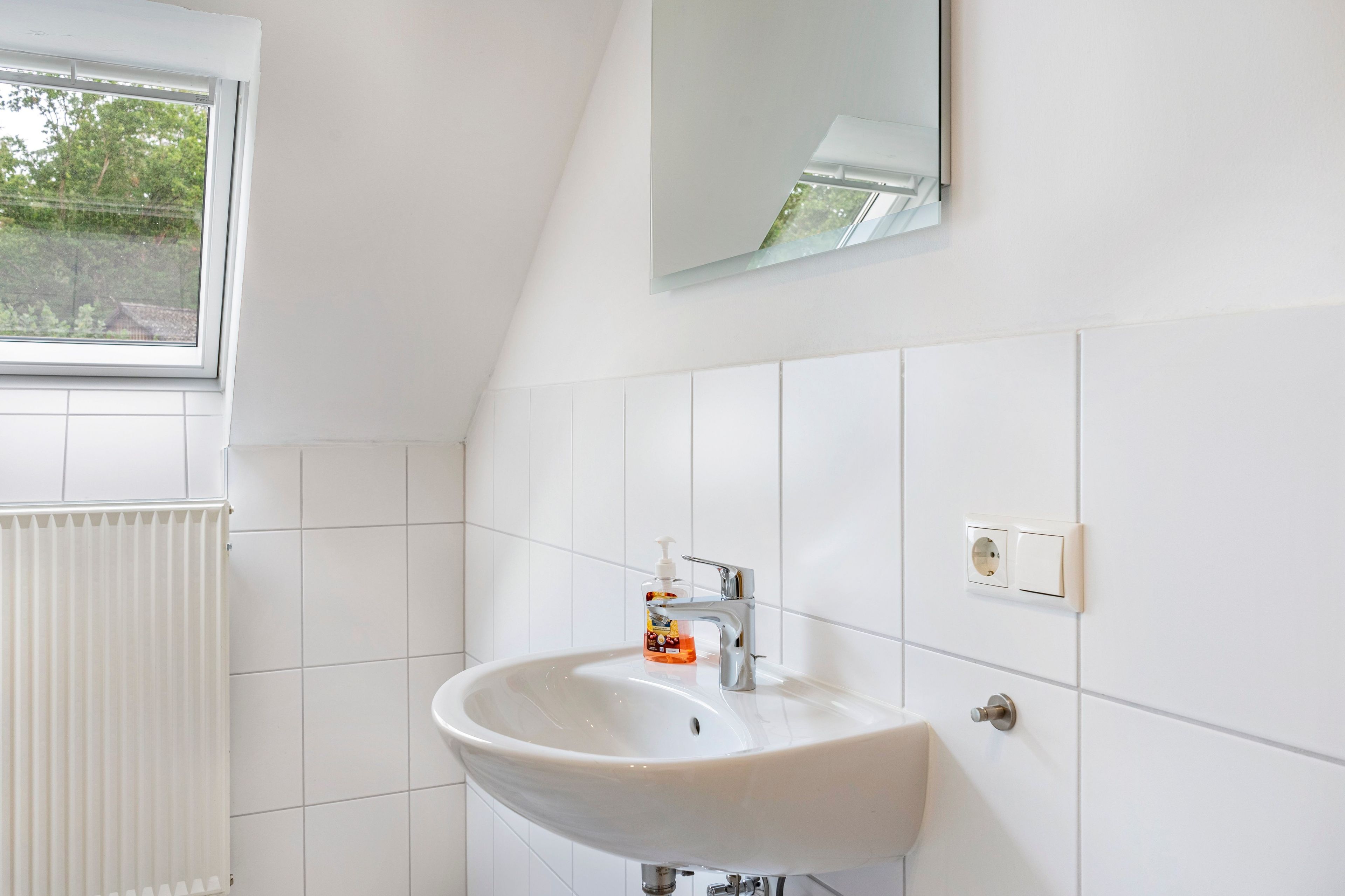 A bathroom with a white sink, a mirror, and a window.