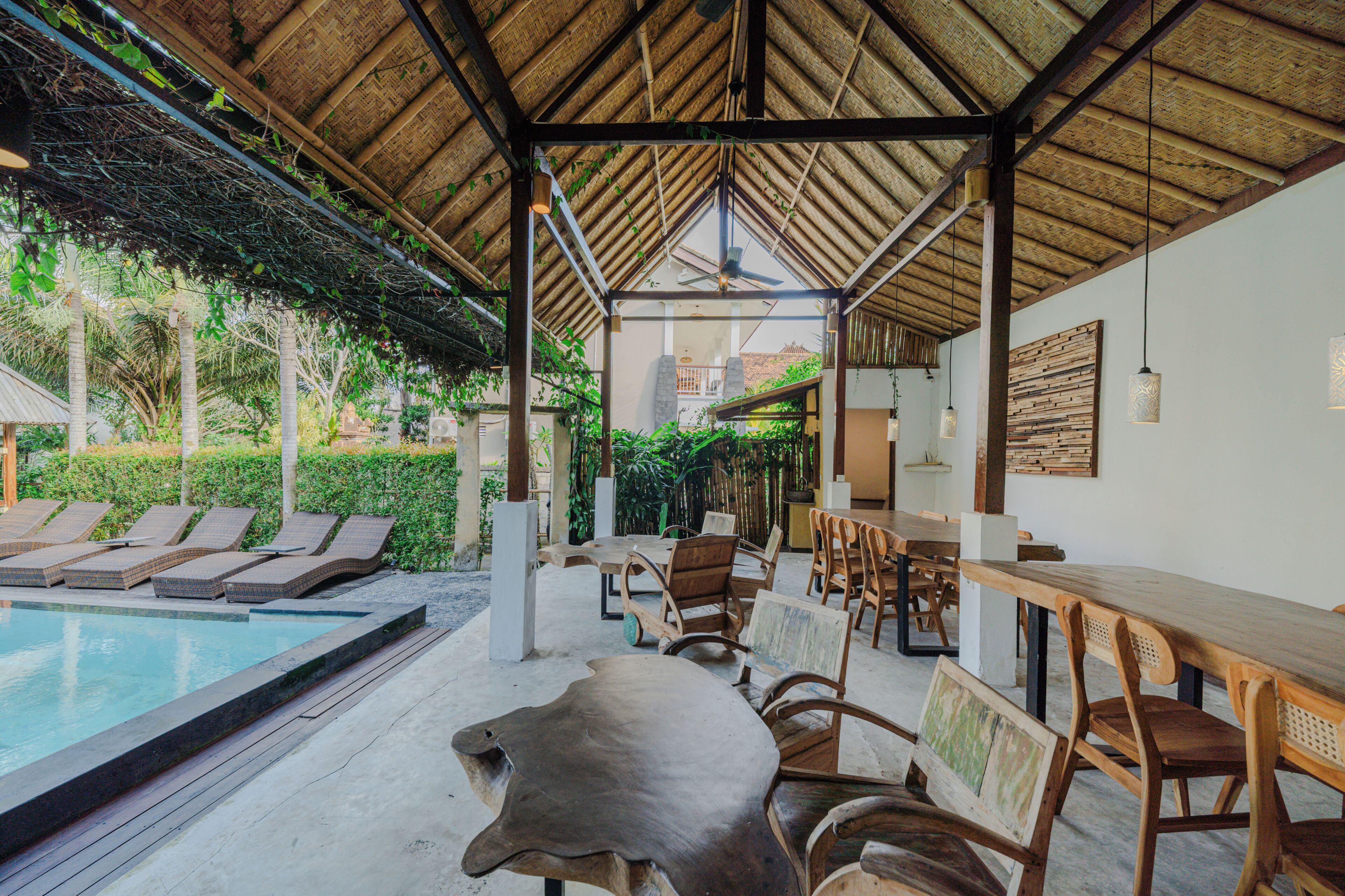 A poolside area with lounge chairs, wooden tables, and a ceiling fan.
