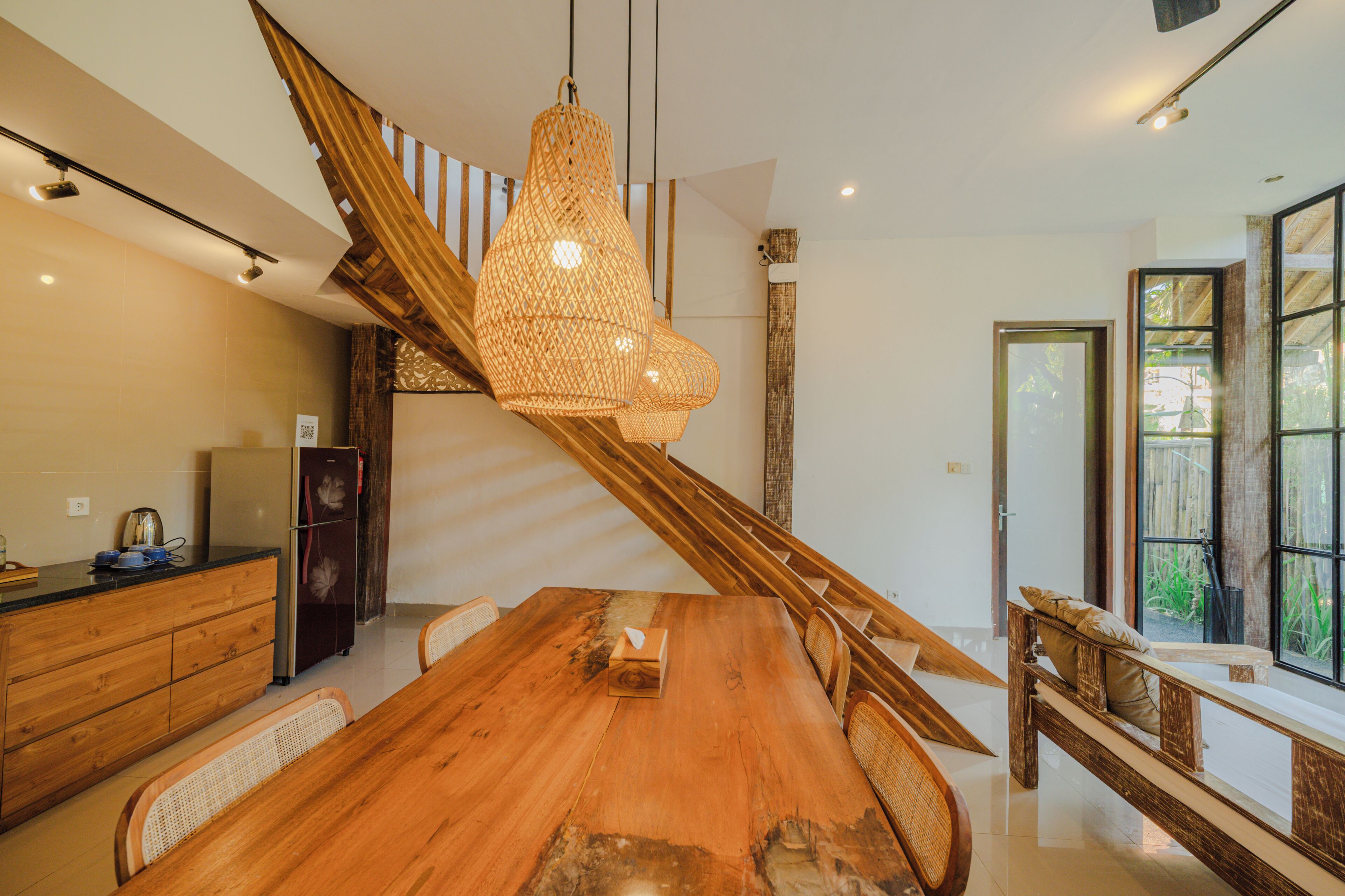 A modern kitchen with a wooden dining table, a built-in refrigerator, and a staircase with a wooden railing.