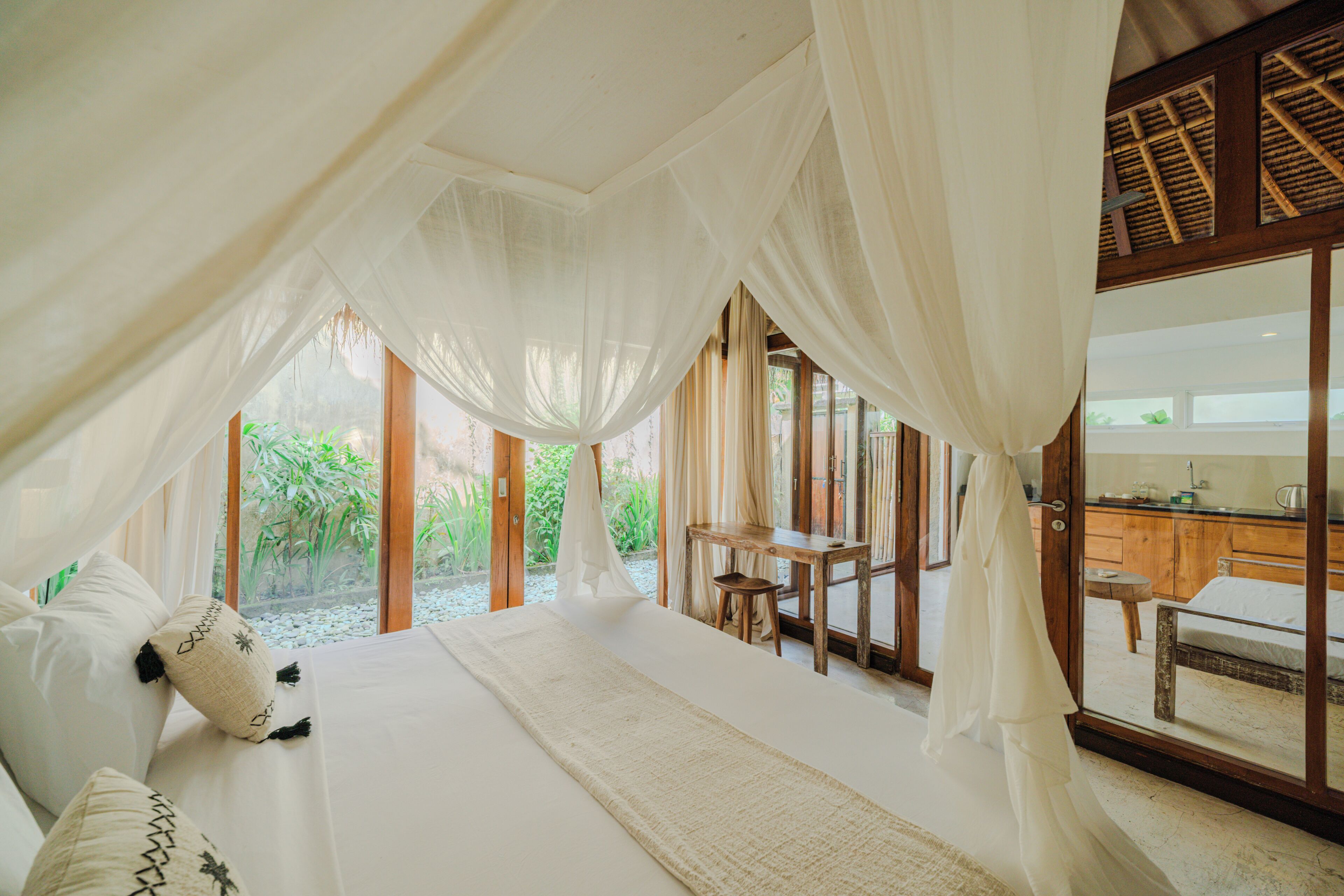A bedroom with a canopy bed, a view of the garden, and a wooden desk.