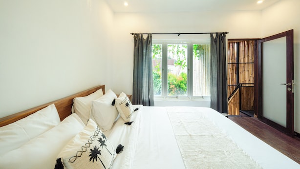 A bedroom with a large bed, a wooden door, and a view of greenery outside.