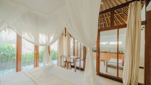 A bedroom with a large bed, a wooden desk, and a view of a garden through a glass door.