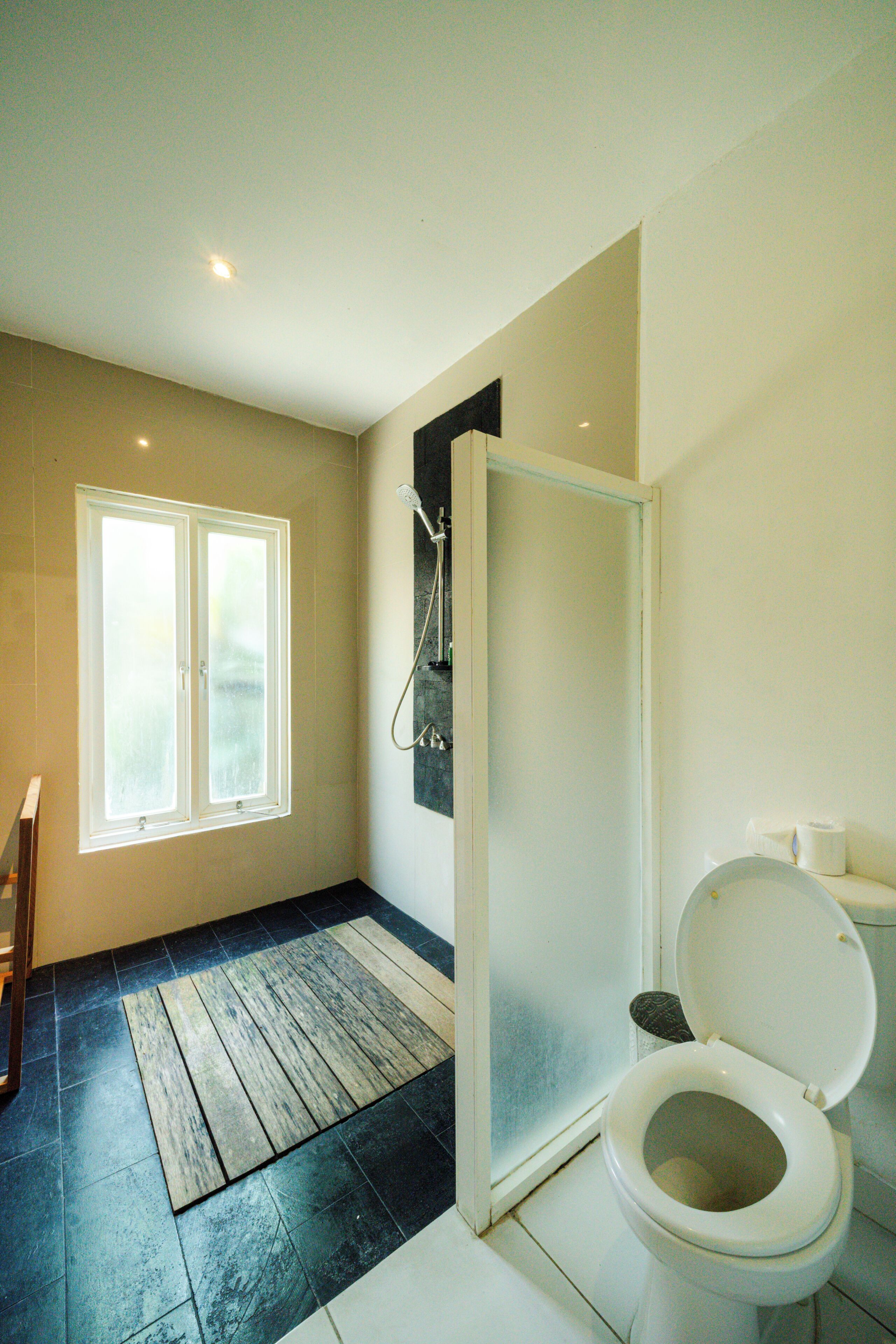 A bathroom with a shower, toilet, and a window.