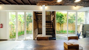 A spacious room with a large wooden table, a built-in bookshelf, and a staircase leading to a balcony.