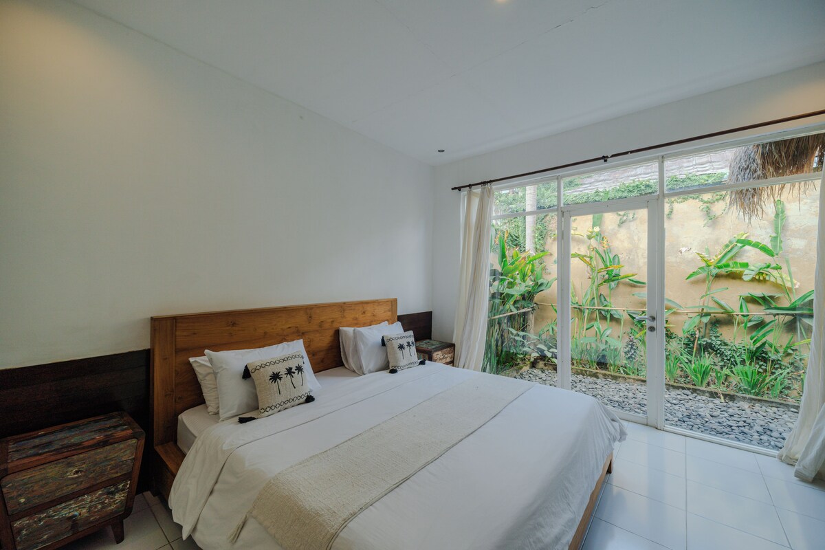A bedroom with a large bed, wooden headboard, and a view of a garden through a glass door.