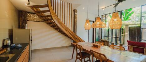 A modern kitchen with a wooden staircase, a dining area with a large table and chairs, and a ceiling fan.