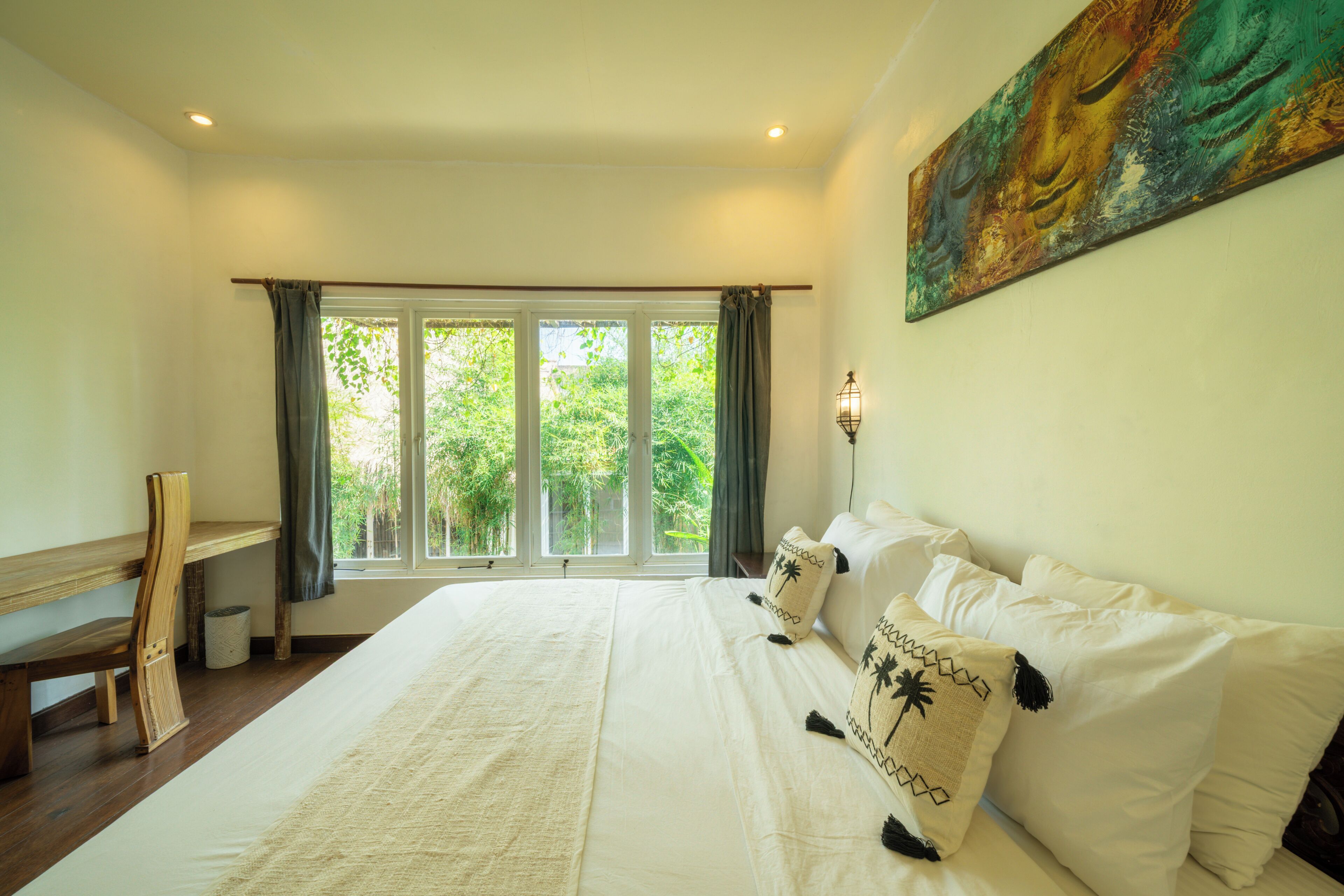 A bedroom with a large bed, a desk, and a window with curtains.