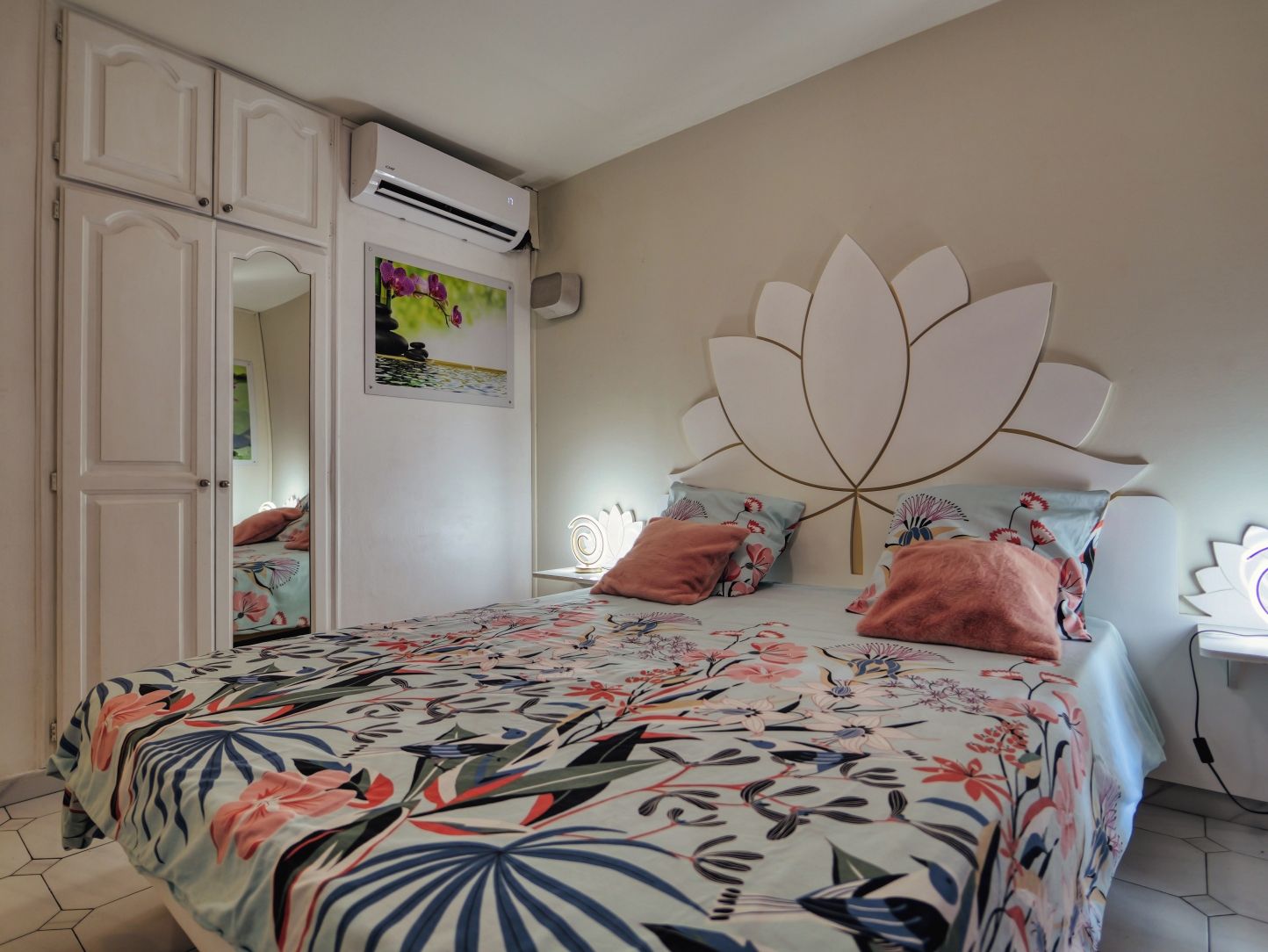 A bedroom with a bed, a wardrobe, an air conditioning unit, and a decorative headboard.