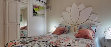 A bedroom with a bed, a wardrobe, an air conditioning unit, and a decorative headboard.
