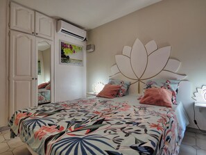 Quarto com cama, guarda-roupa, ar condicionado e cabeceira decorativa.