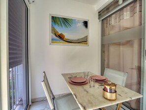 A dining area with a table set for two, a hammock painting on the wall, and a view through a glass door. - Ocean view, close to all amenities (Saint-François)