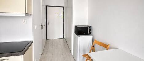 A compact kitchen with a microwave, refrigerator, and a small dining table with a chair.