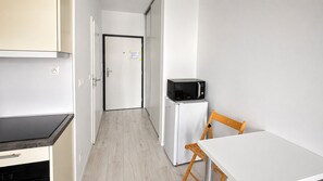 A compact kitchen with a microwave, refrigerator, and a small dining table with a chair. - 1 room apartment, balcony, Zuzany Chalupovej 18 (Bratislava)