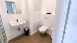 A bathroom with a sink, toilet, and a trash bin.