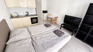 A modern bedroom with a bed, a TV, a desk, and a kitchenette.
