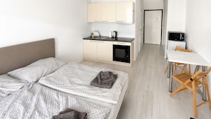 A hotel room with a bed, a small kitchenette, a dining table with chairs, and a door leading to another room.