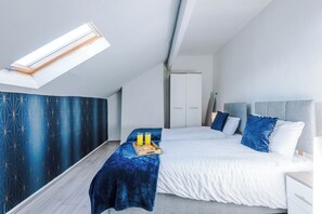 Quarto moderno com claraboia, cama com roupa de cama azul, mesa de cabeceira e guarda-roupa.