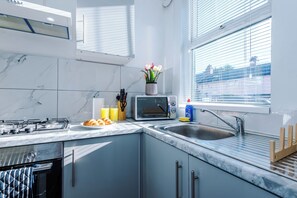Uma cozinha moderna com fogão a gás, forno embutido, pia e janela com persianas.