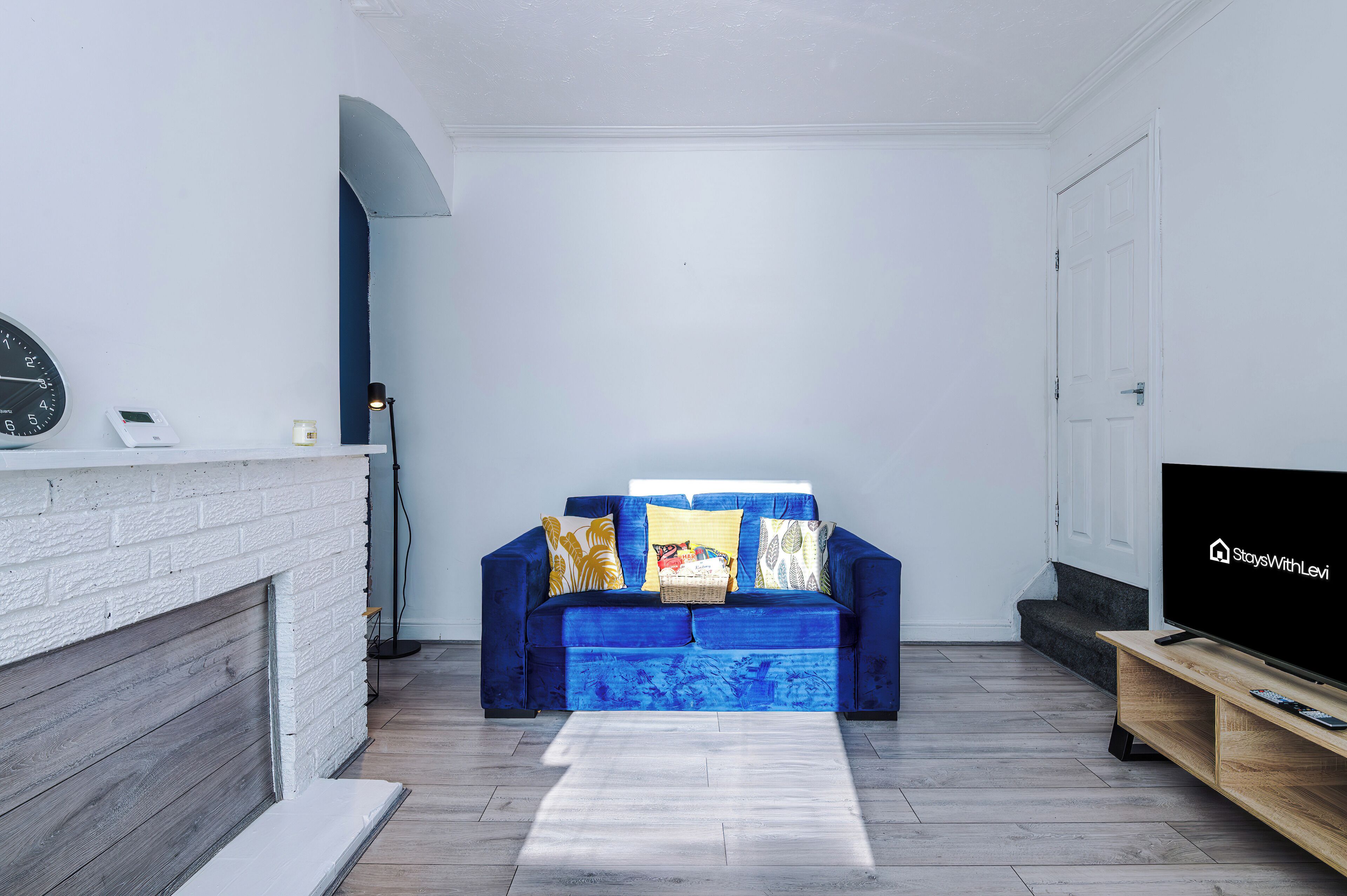 A living room with a blue sofa, a flat-screen TV, a fireplace, and a clock on the wall.