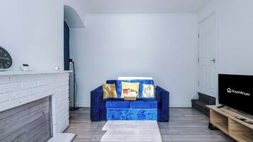 A living room with a blue sofa, a flat-screen TV, a fireplace, and a clock on the wall.
