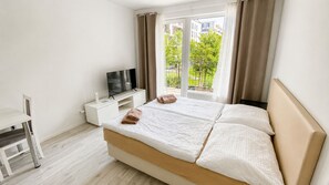Une chambre d’hôtel avec un lit, une télévision, un bureau et une fenêtre avec des rideaux.
