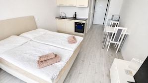 Quarto de hotel com uma cama, uma kitchenette pequena, uma mesa e uma cadeira.