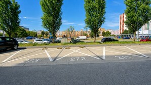 Um estacionamento com vagas demarcadas, árvores e edifícios ao fundo.