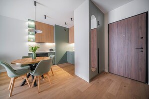 A modern kitchen with wooden cabinets, a dining table with chairs, and a large wooden door. - Kierbedzia Prestige, Mokotów (Warszawa)