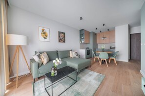 Un salon moderne avec un canapé, une table basse et un coin repas avec des chaises. On aperçoit une cuisine à l’arrière-plan, avec des placards et une table à manger.
