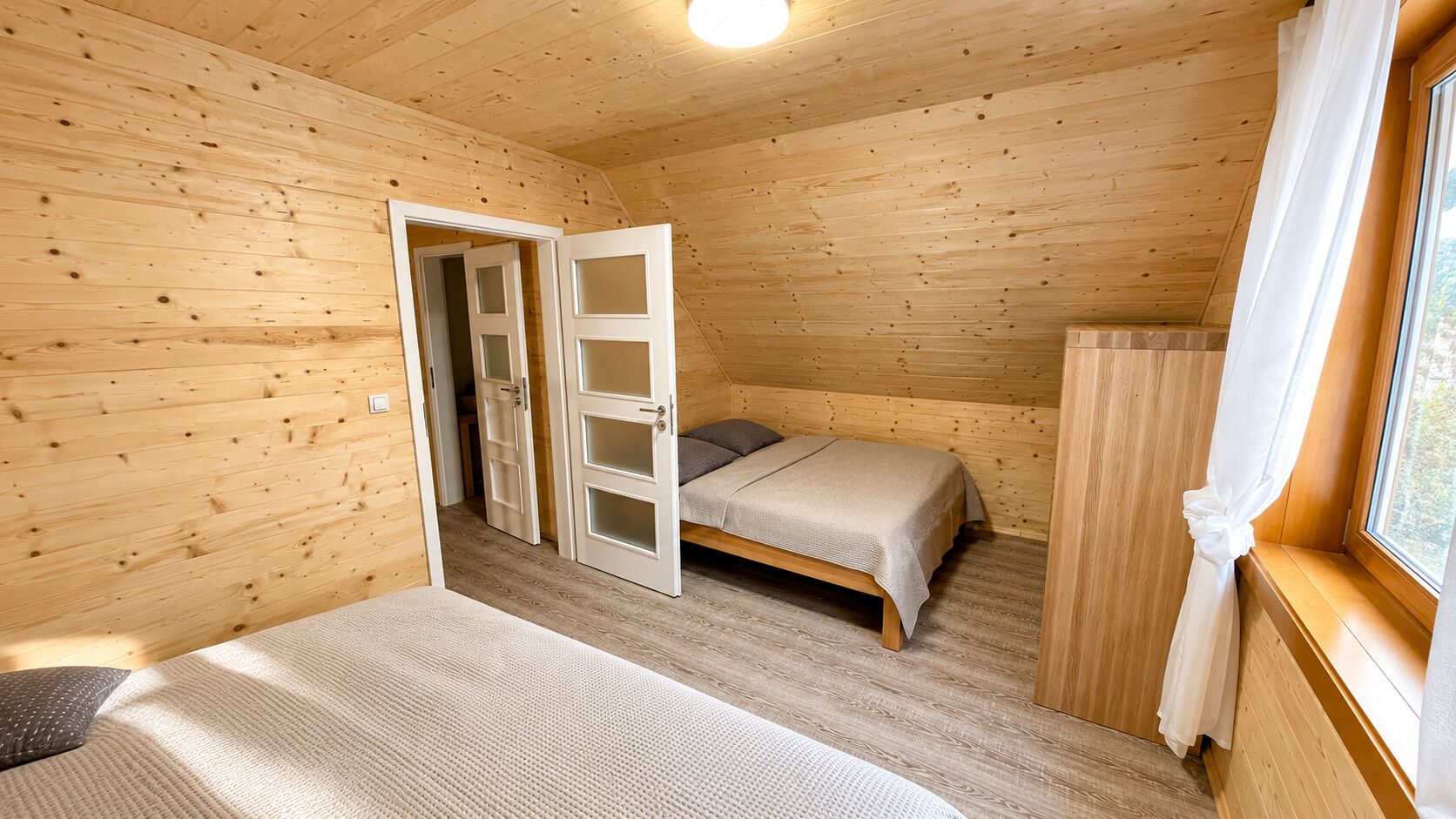 A wooden cabin room with a bed, a small table, and a window with curtains.