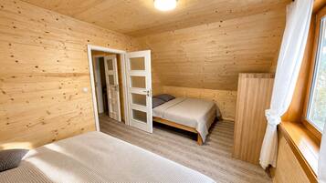 A wooden cabin room with a bed, a small table, and a window with curtains.