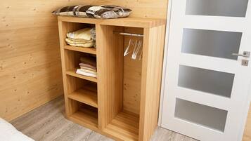 A wooden wardrobe with shelves and hanging space, a white door with frosted glass panels, and a patterned cushion on top.