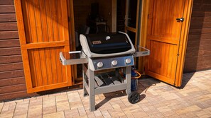 A Weber Spirit II grill with a side table and a gas tank, positioned outside a wooden building with a sliding door.