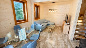 A cozy cabin interior with a glass dining table, blue upholstered sofa, and a wooden staircase.