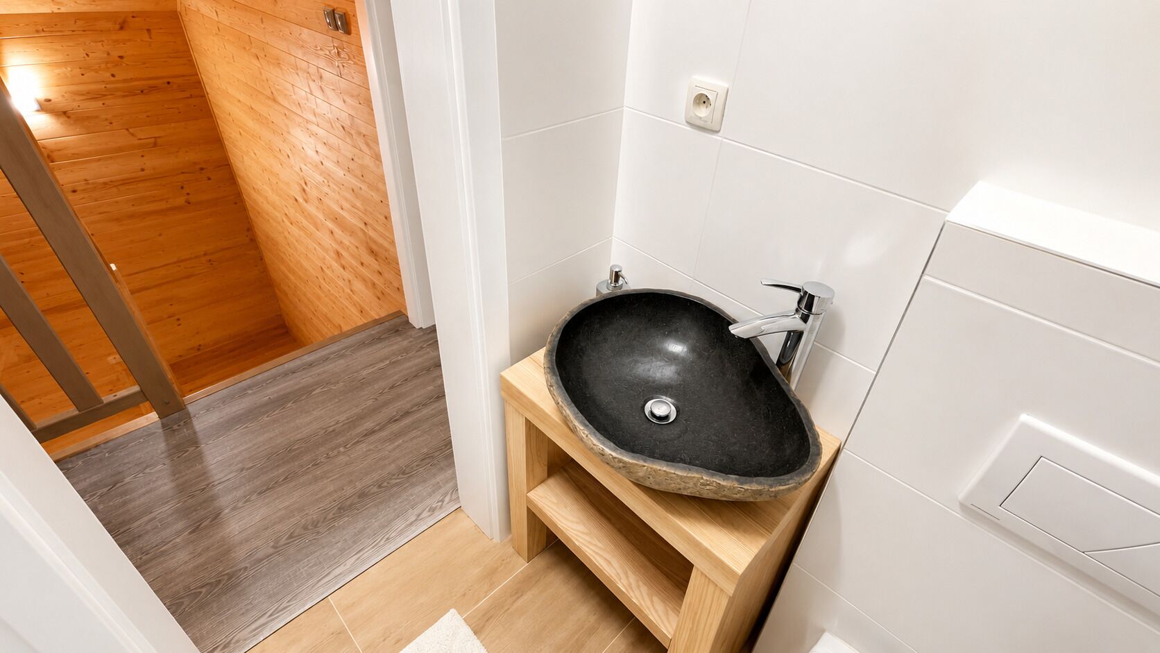 A bathroom with a wooden floor, a black sink, and white tiled walls.