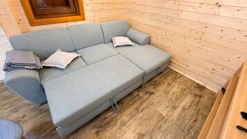 Ein hellgraues Sofa mit zwei Kissen und einer zusammengefalteten Decke in einem Raum mit Holzwandverkleidung und Holzboden.