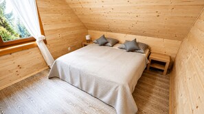 Un dormitorio de cabaña de madera con cama, almohadas, mesita de noche y una ventana con cortinas.