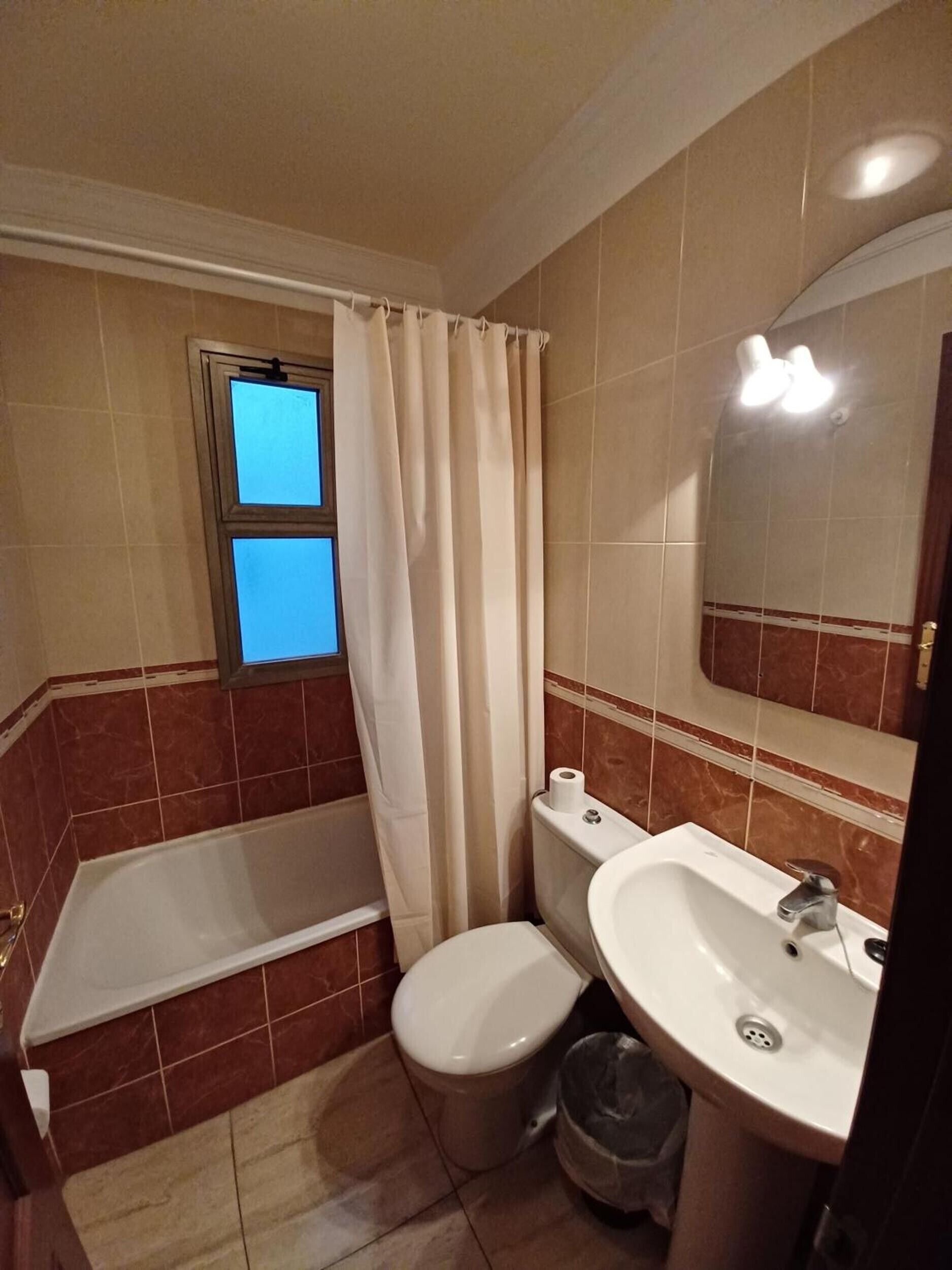 Een badkamer met een bad, toilet, wastafel en een raam met gordijn.
