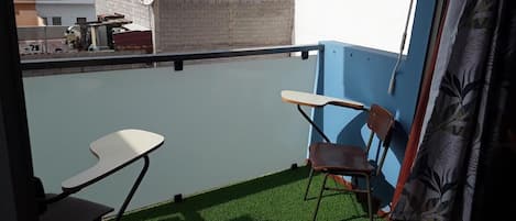 Un balcon avec deux chaises et une petite table, un sol recouvert d’un gazon artificiel vert, et une vue sur le paysage urbain.