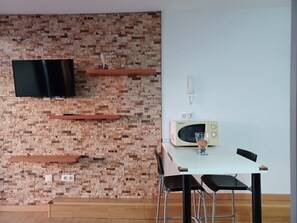 A modern kitchen with a brick wall, a flat-screen TV, a microwave, and a dining table with chairs.