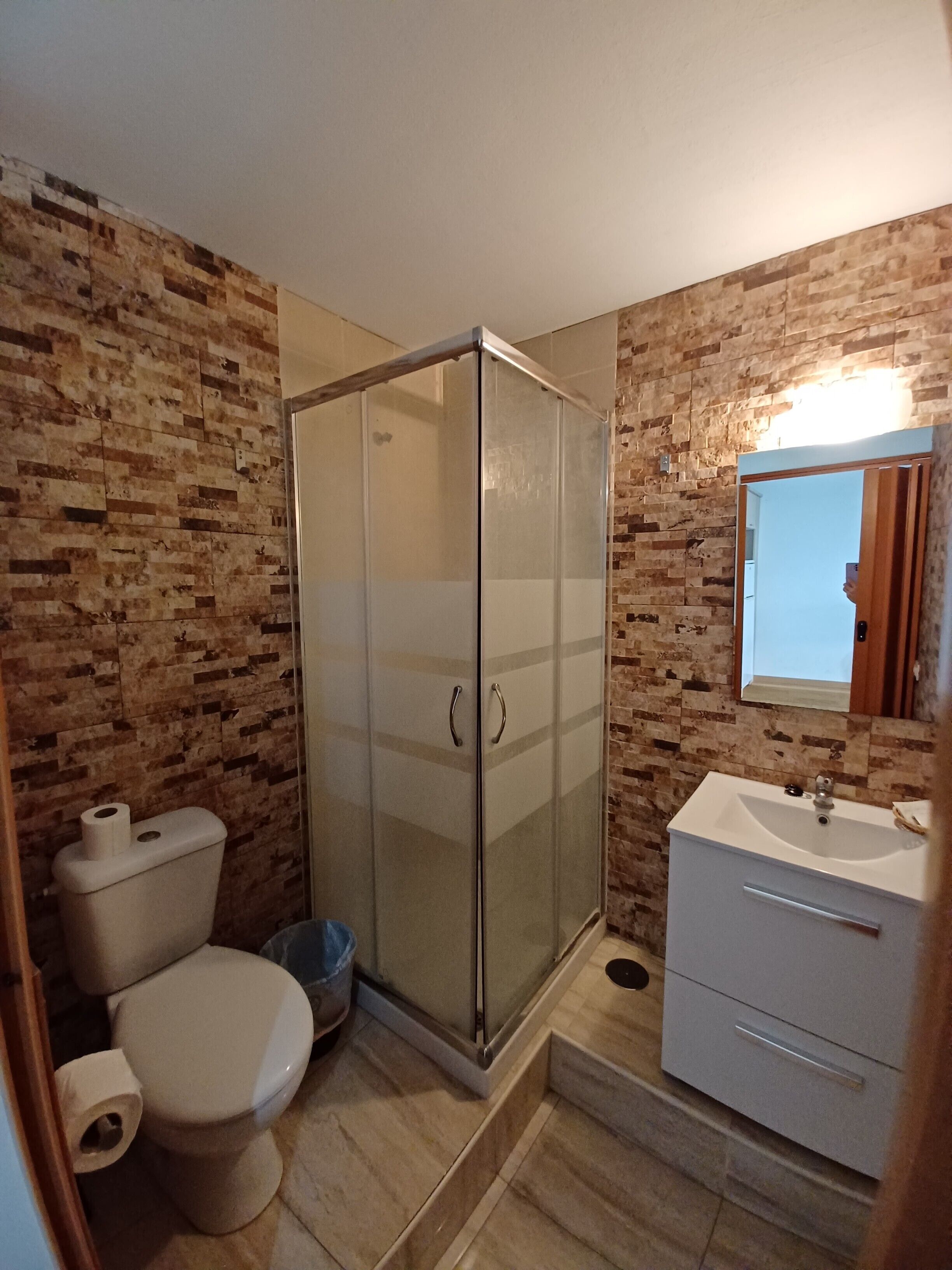 Een badkamer met een douche met glazen wand, toilet, wastafel en spiegel.
