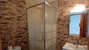 Et badeværelse med en glasafskærmet brusekabine, toilet, vask og spejl.