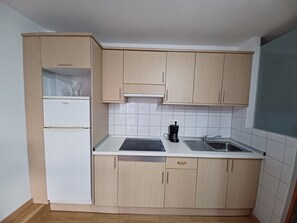 Eine kompakte Küche mit hellen Holzschränken, einem weißen Kühlschrank, einer Kaffeemaschine und einem Spülbecken.